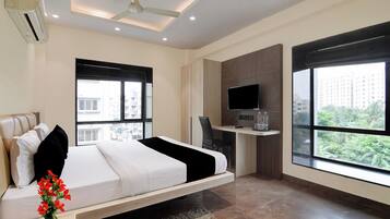 A modern hotel room with a bed, a desk, a TV, and large windows.