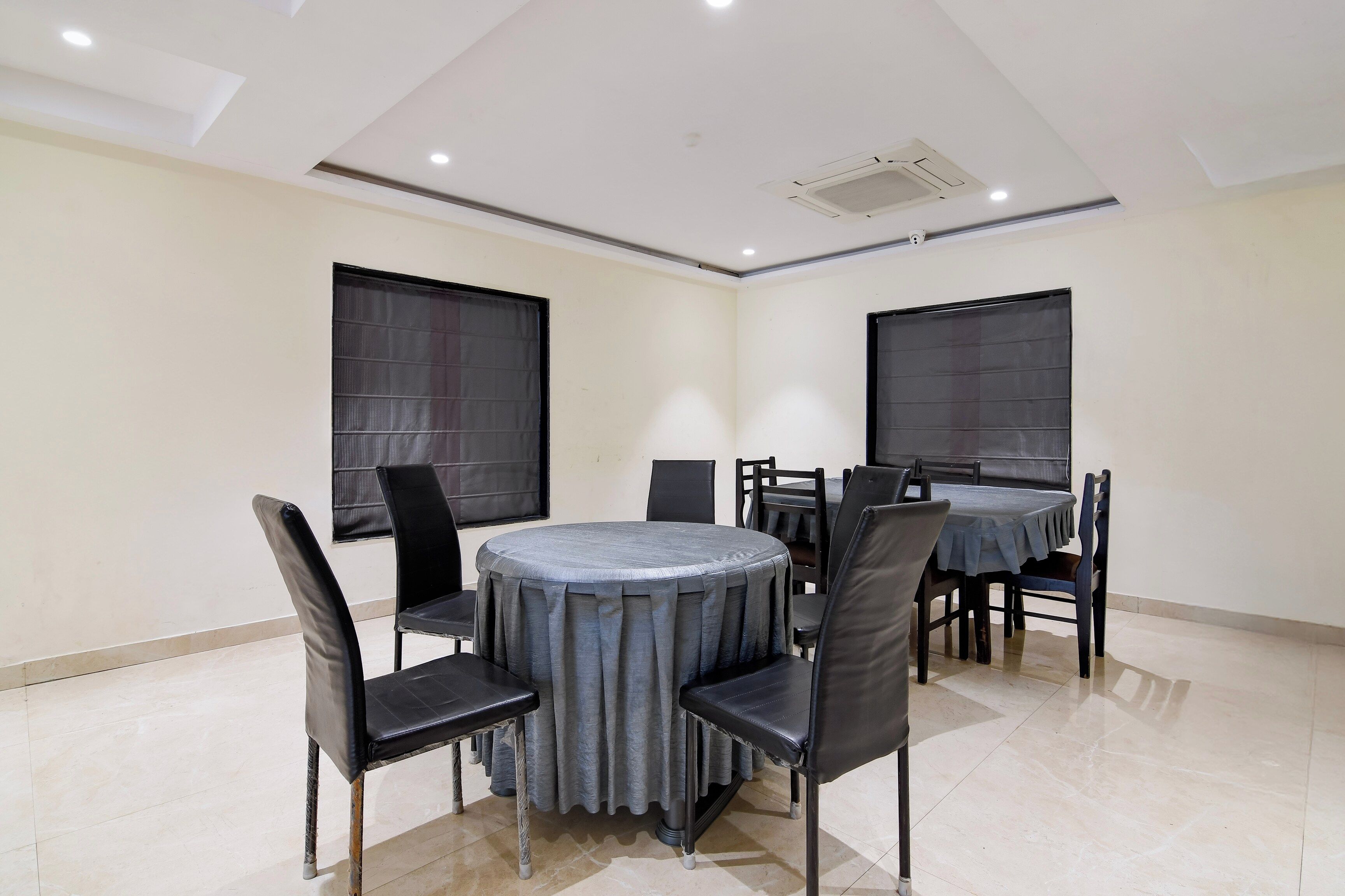 A conference room with a round table, black chairs, and large windows with blinds.