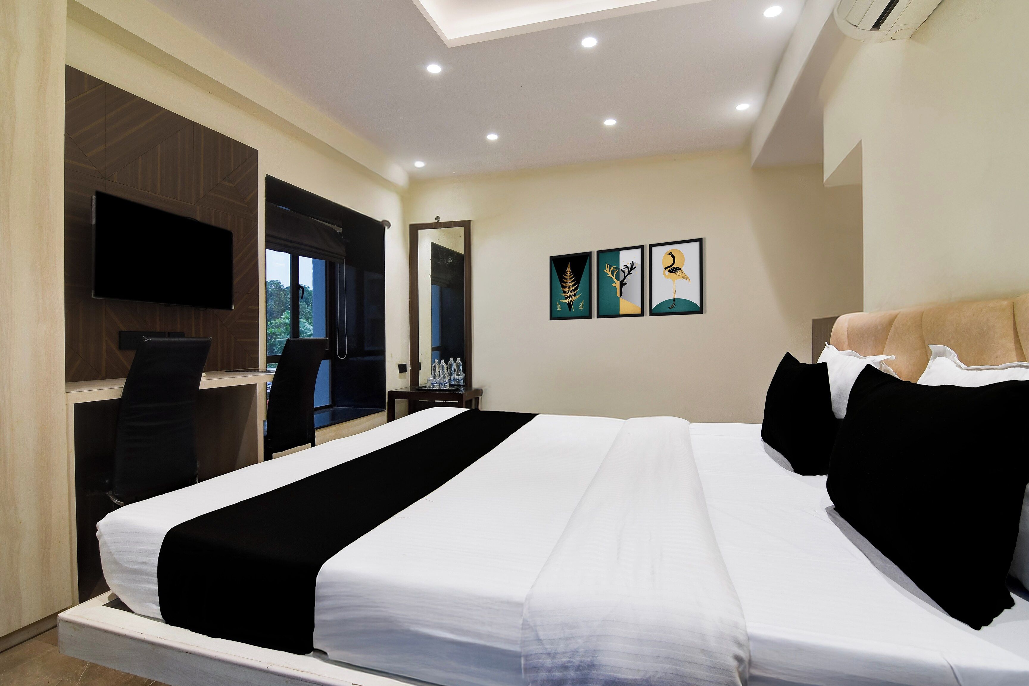 Una habitación de hotel con cama, escritorio, televisión y cuadros en la pared.