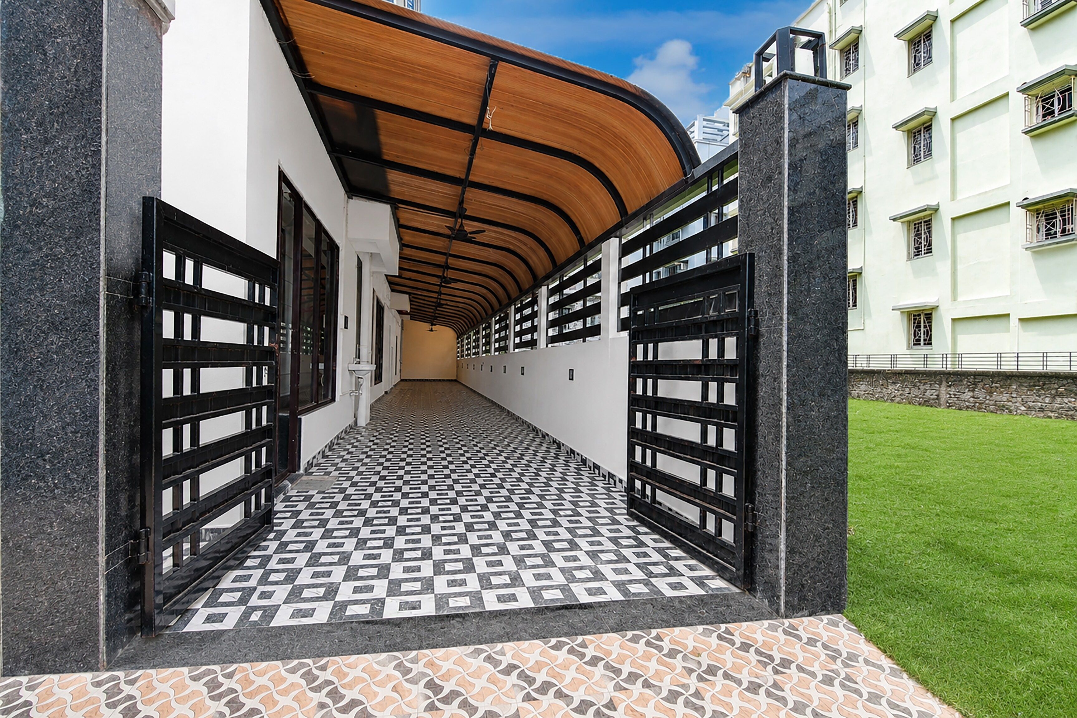 A corridor with patterned flooring, a curved wooden ceiling, and a view of a building with multiple windows.