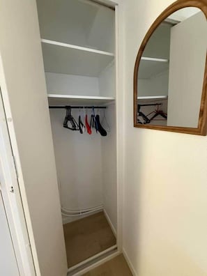 Ein kleiner begehbarer Kleiderschrank mit Spiegel und Ablage für Kleidung.
