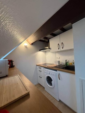 Eine kompakte Küche mit integriertem Waschmaschine, einer Holz Arbeitsplatte und weißen Schränken.