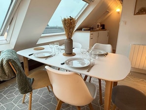 Ein Essbereich mit einem Tisch für zwei Personen, einer Vase mit getrockneten Blumen und Blick auf das Meer durch ein Oberlicht.