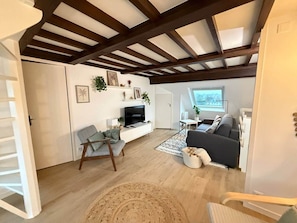 Ein offener Wohnbereich mit Holzboden, einer Couch, einem Fernseher und einer Treppe.
