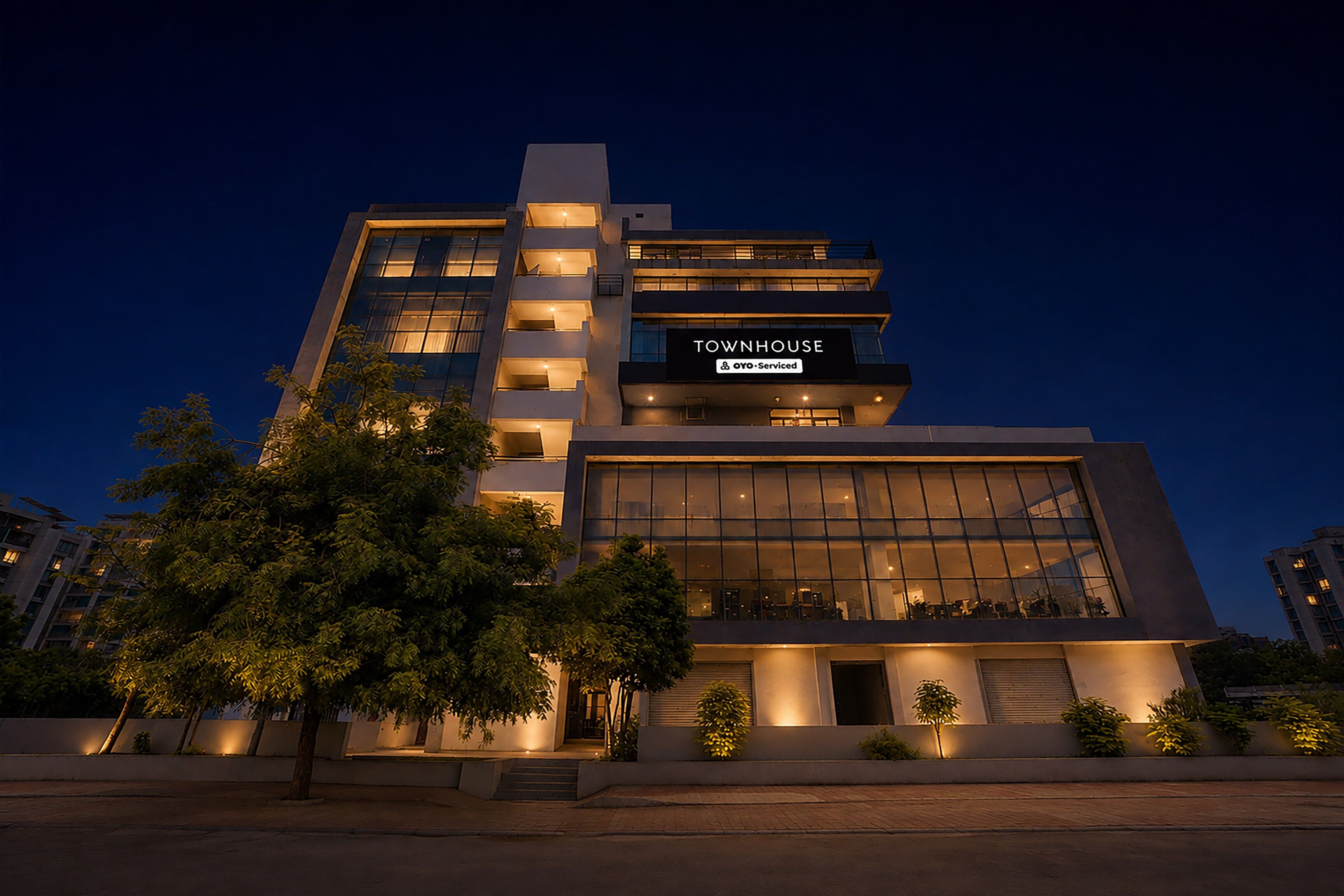 A modern townhouse with a prominent 'TOWNHOUSE' sign, multiple balconies, and a well-lit facade.
