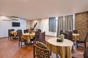 A dining area with round tables, chairs, and a brick accent wall. - Townhouse Chandlodiya Railway Station (Ahmedabad)