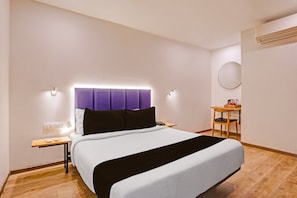 Quarto de hotel com cama, mesa de cabeceira e pequena escrivaninha com cadeira.
