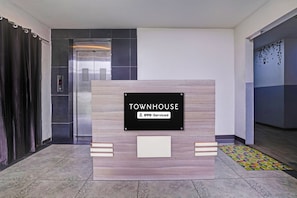 Bancada de recepção com uma placa indicando 'TOWNHOUSE YO0-Serviced' em um hall moderno com elevador e ladrilhos estampados.