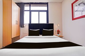 A hotel room with a bed, a nightstand, a vase with flowers, a window with curtains, and a framed picture on the wall. - Townhouse Chandlodiya Railway Station (Ahmedabad)