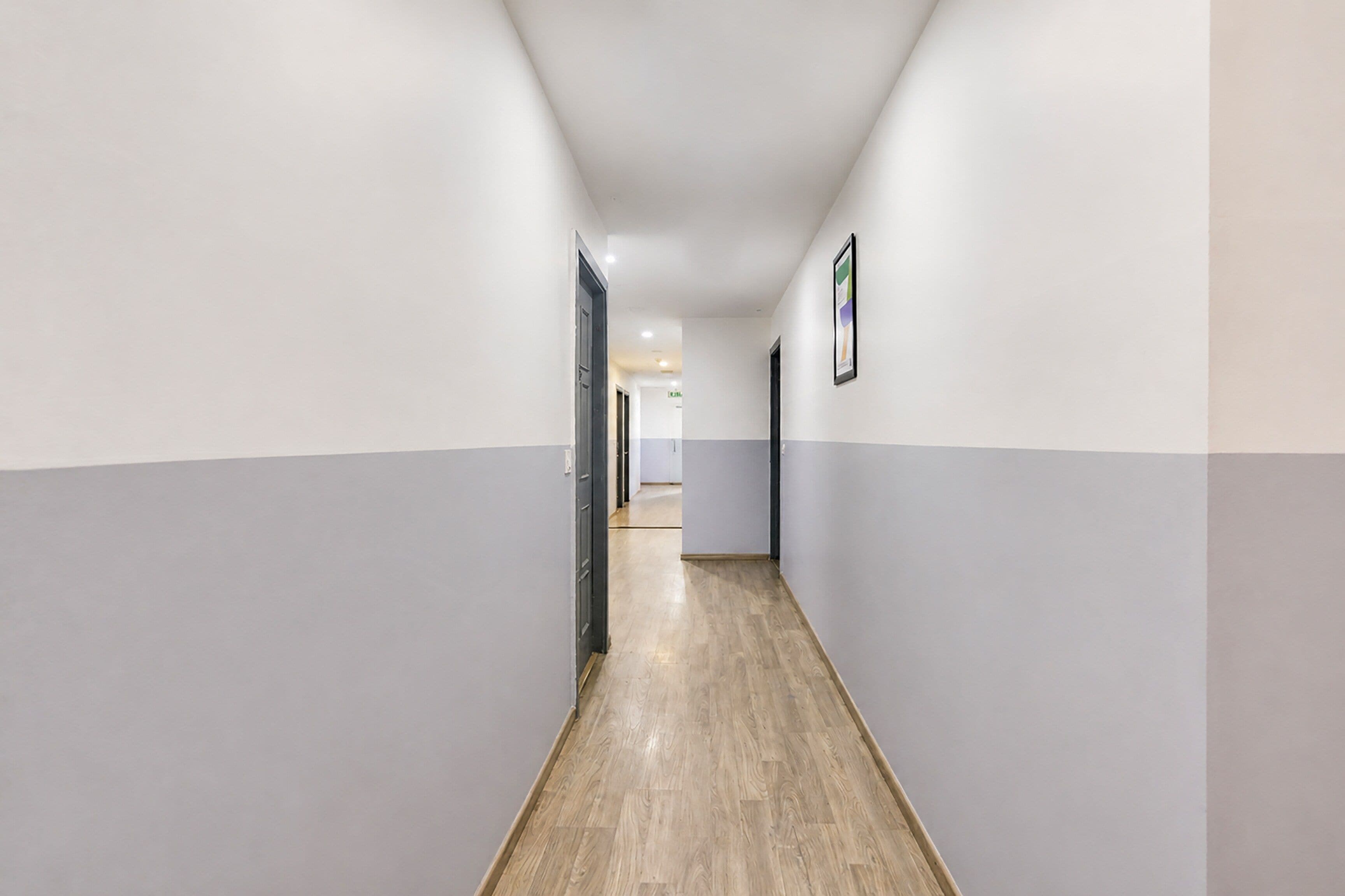 A corridor with a wooden floor, white walls, and doors on both sides.