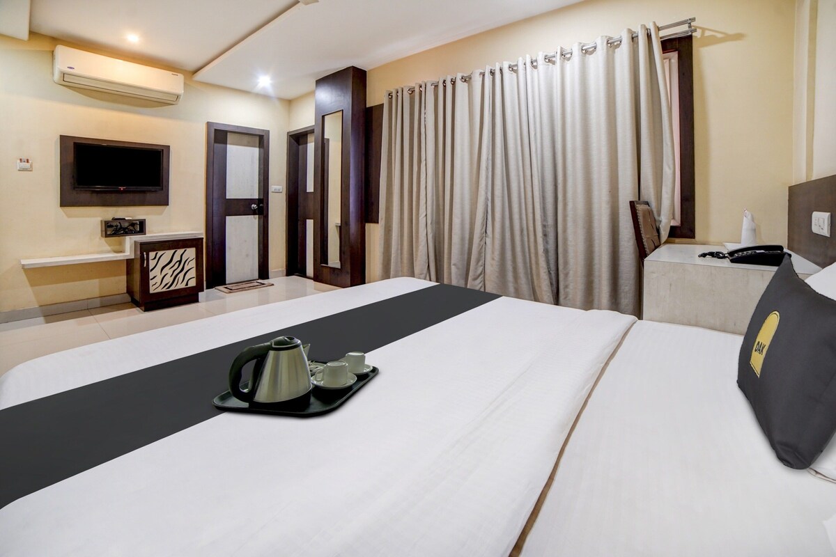Una camera d'albergo con un letto, un comodino, una TV, uno specchio, una tenda e un condizionatore d'aria fissato al muro.