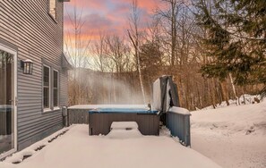 Een sneeuwwitte jacuzzi in een achtertuin, met een huis en bomen op de achtergrond.