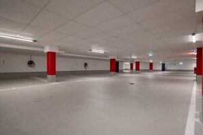 A multi-level parking garage with white and red pillars, marked parking spaces, and overhead fluorescent lighting. - Holiday apartment with 1 bedroom (Ostseebad Zingst)