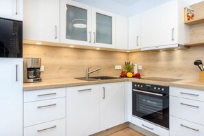 A modern kitchen with white cabinets, a built-in oven, a coffee maker, and a fruit bowl. - Holiday apartment with 1 bedroom (Ostseebad Zingst a Darß)