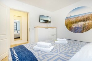 A hotel room with a bed, a circular wall decoration, a bedside table with a lamp, and a view of the beach through the window. - Holiday apartment with 1 bedroom (Ostseebad Zingst a Darß)