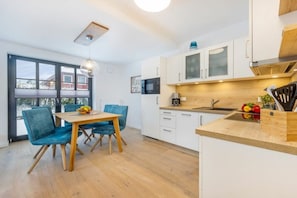 A modern kitchen with white cabinets, a wooden countertop, and a dining area with blue chairs. - Holiday apartment with 1 bedroom (Ostseebad Zingst a Darß)