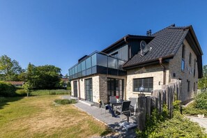 A modern two-story house with a glass extension, a patio with outdoor furniture, and a well-maintained lawn. - Holiday apartment with 1 bedroom (Ostseebad Zingst a Darß)