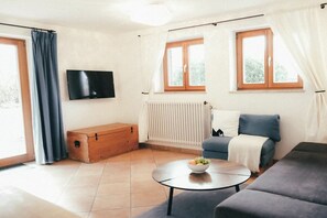A modern living room with a sofa, a coffee table with fruit, a television, and a window with curtains. - House Luna - Apartment Luna 1 (Schwangau)