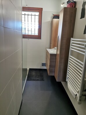 Een badkamer met een douche, een raam, een radiator en een handdoekrek.