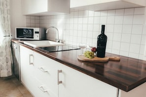 Une cuisine équipée d’un four à micro-ondes, d’un évier et d’une planche à découper en bois sur laquelle se trouvent des raisins et une bouteille.