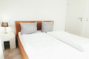 A single bed with a white mattress and two pillows, a bedside table with a lamp, and a white door. - House Luna - Apartment Luna 2 (Schwangau)
