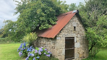 Una cabaña de piedra con techo de metal, una puerta de madera y arbustos de hortensia en primer plano.