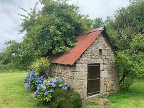 Una cabaña de piedra con techo de metal, una puerta de madera y arbustos de hortensia en primer plano.