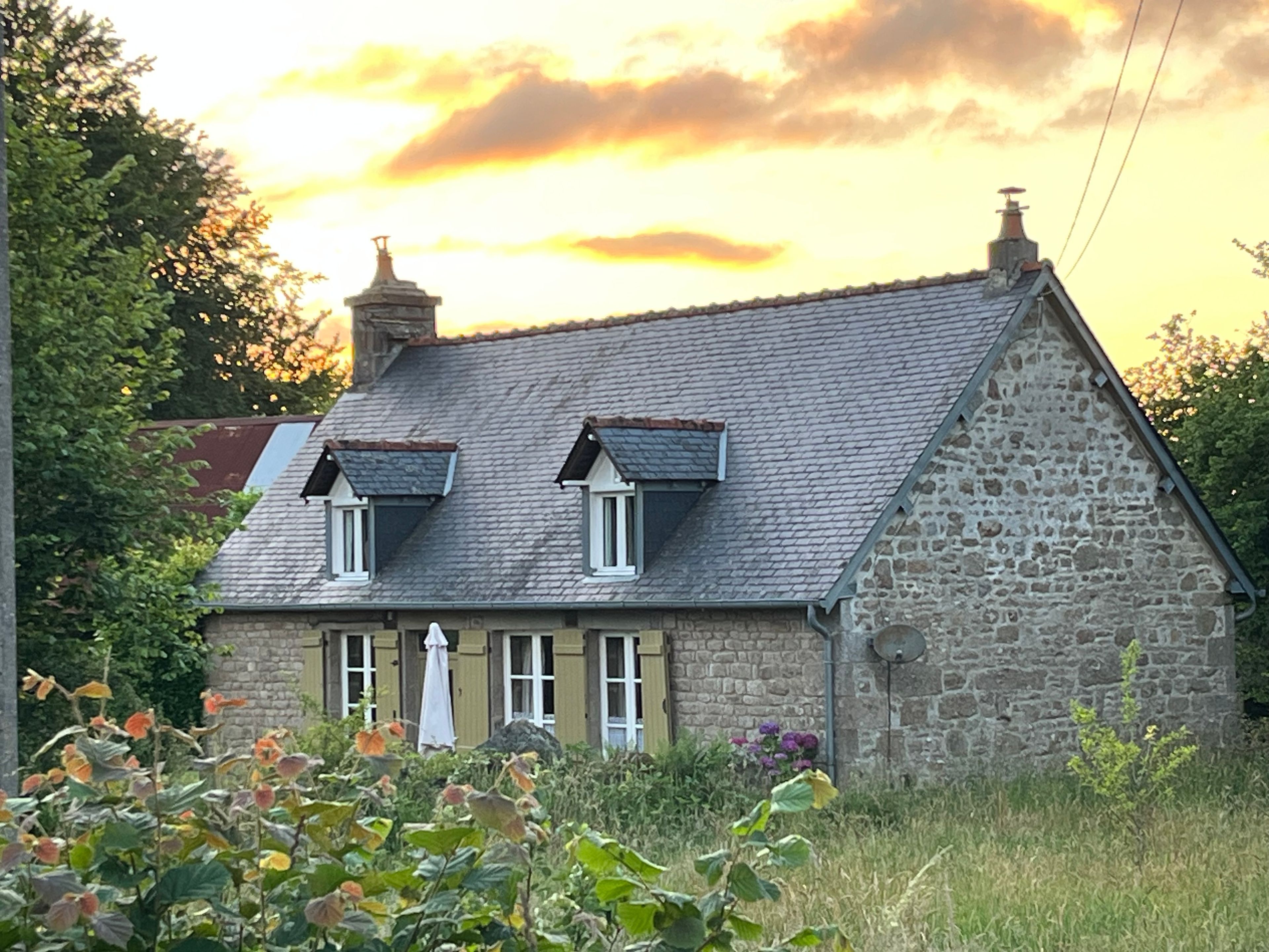 A stone house with a sloped roof, two dormer windows, and a chimney.