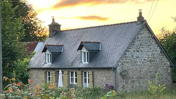 A stone house with a sloped roof, two dormer windows, and a chimney.