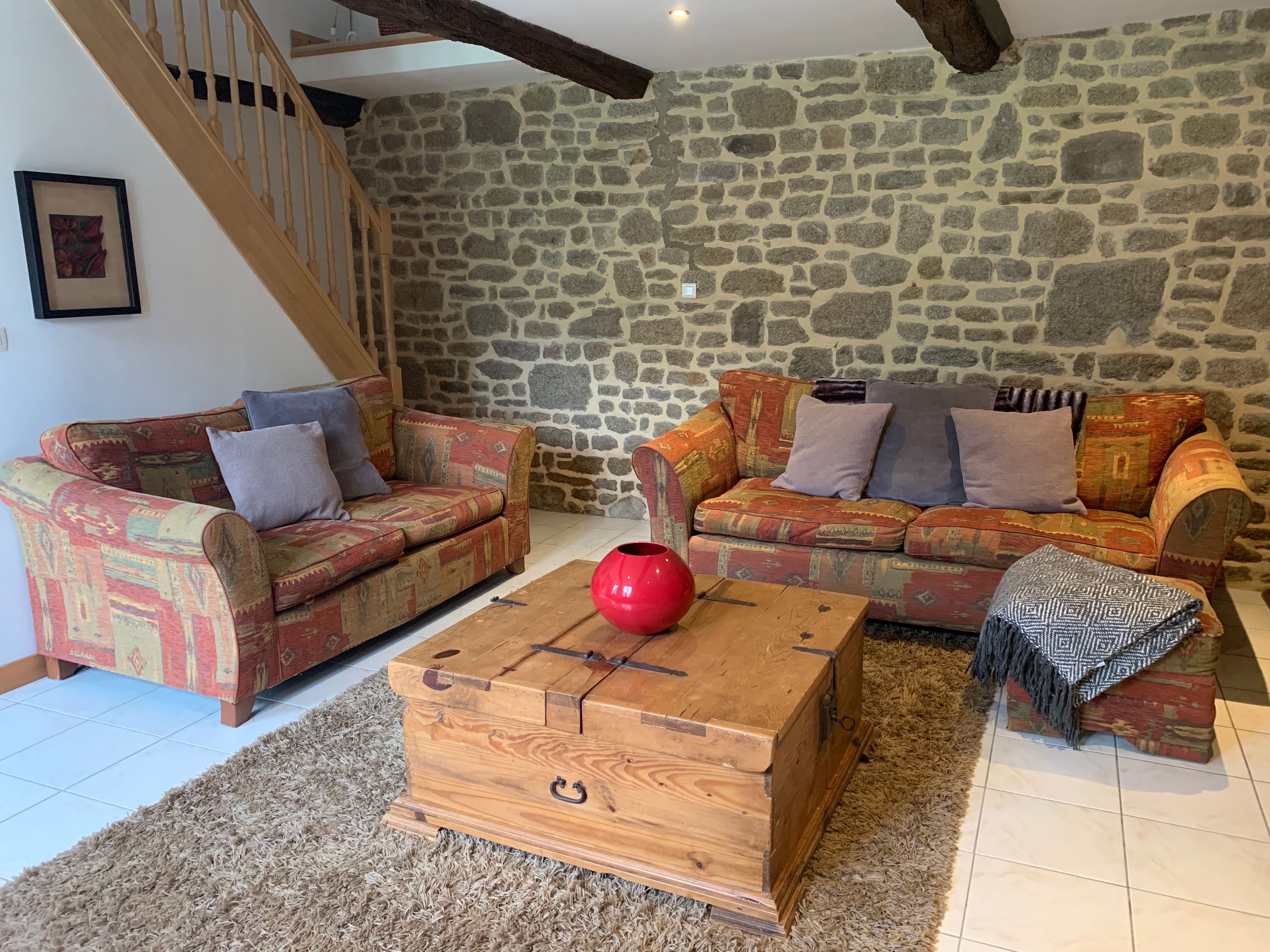 A cozy living room with two patterned sofas, a wooden coffee table, and a stone wall.