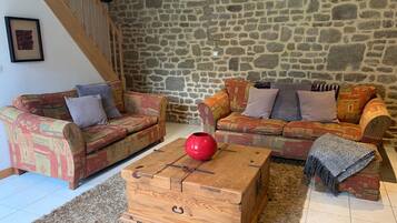 A cozy living room with two patterned sofas, a wooden coffee table, and a stone wall.