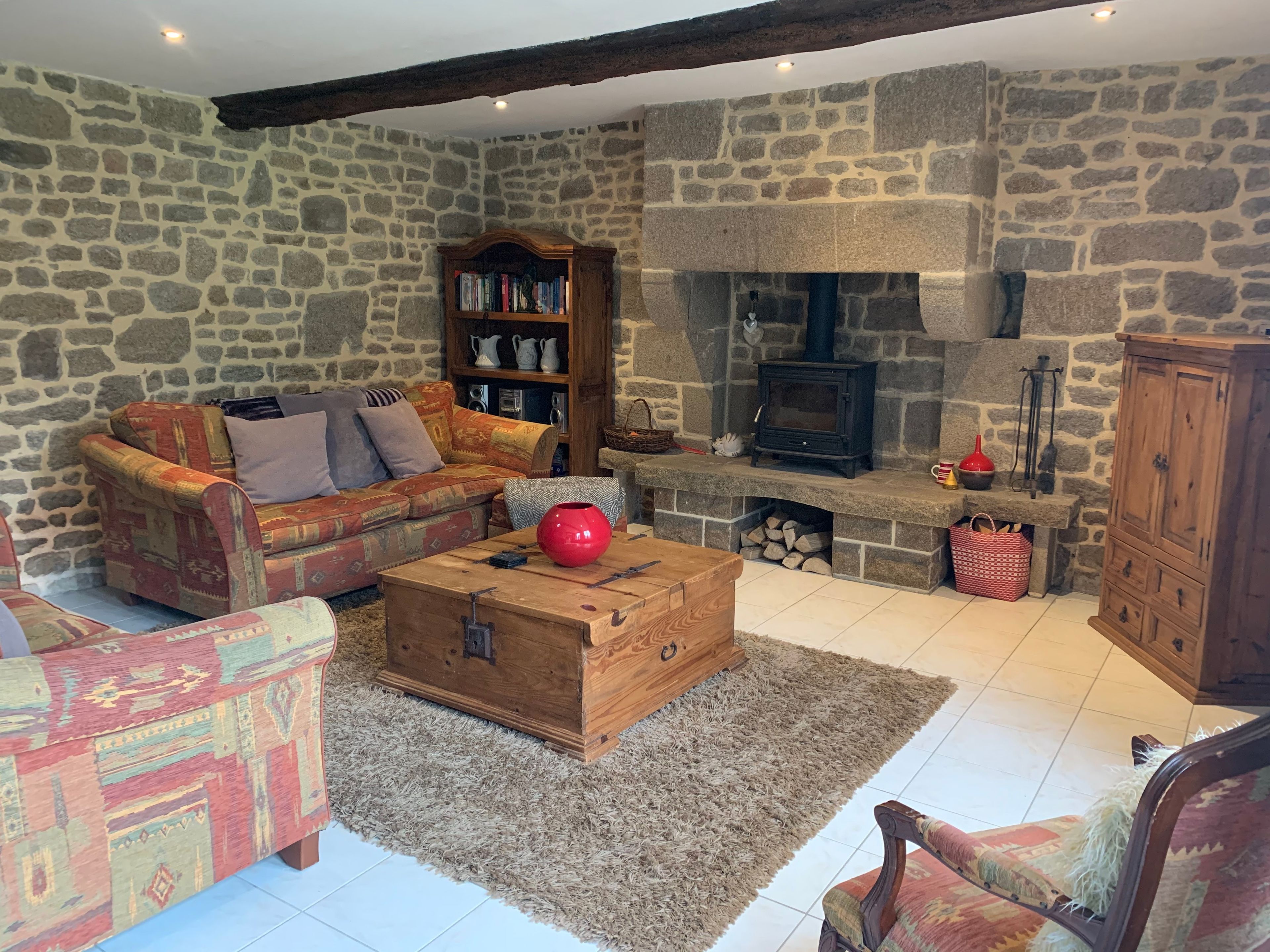 A cozy living room with a stone wall, a fireplace, a sofa, a bookshelf, and a wooden chest.