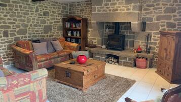 A cozy living room with a stone wall, a fireplace, a sofa, a bookshelf, and a wooden chest.