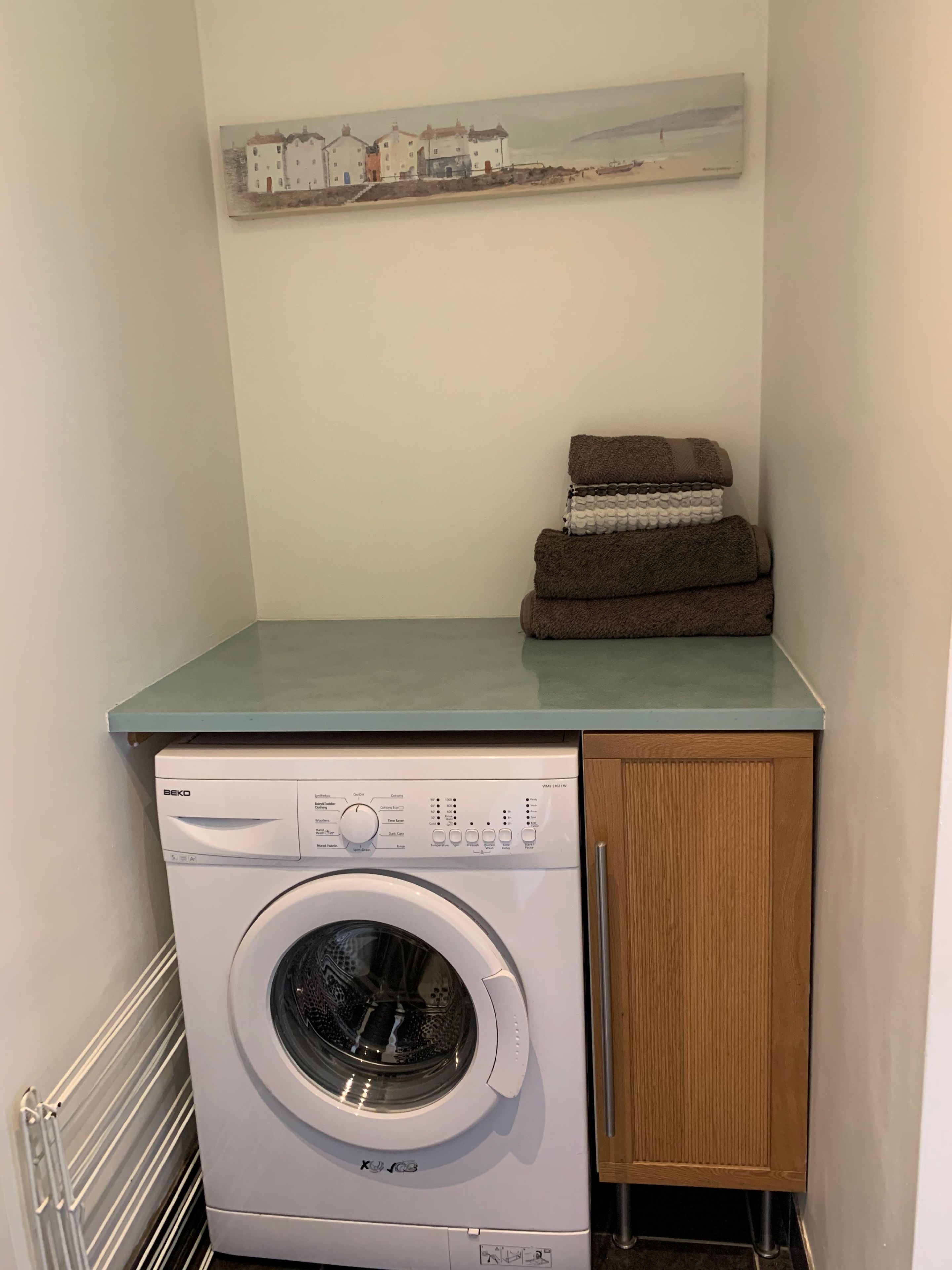 A compact laundry area with a front-loading washing machine, a wooden cabinet, and a towel stack on a countertop.