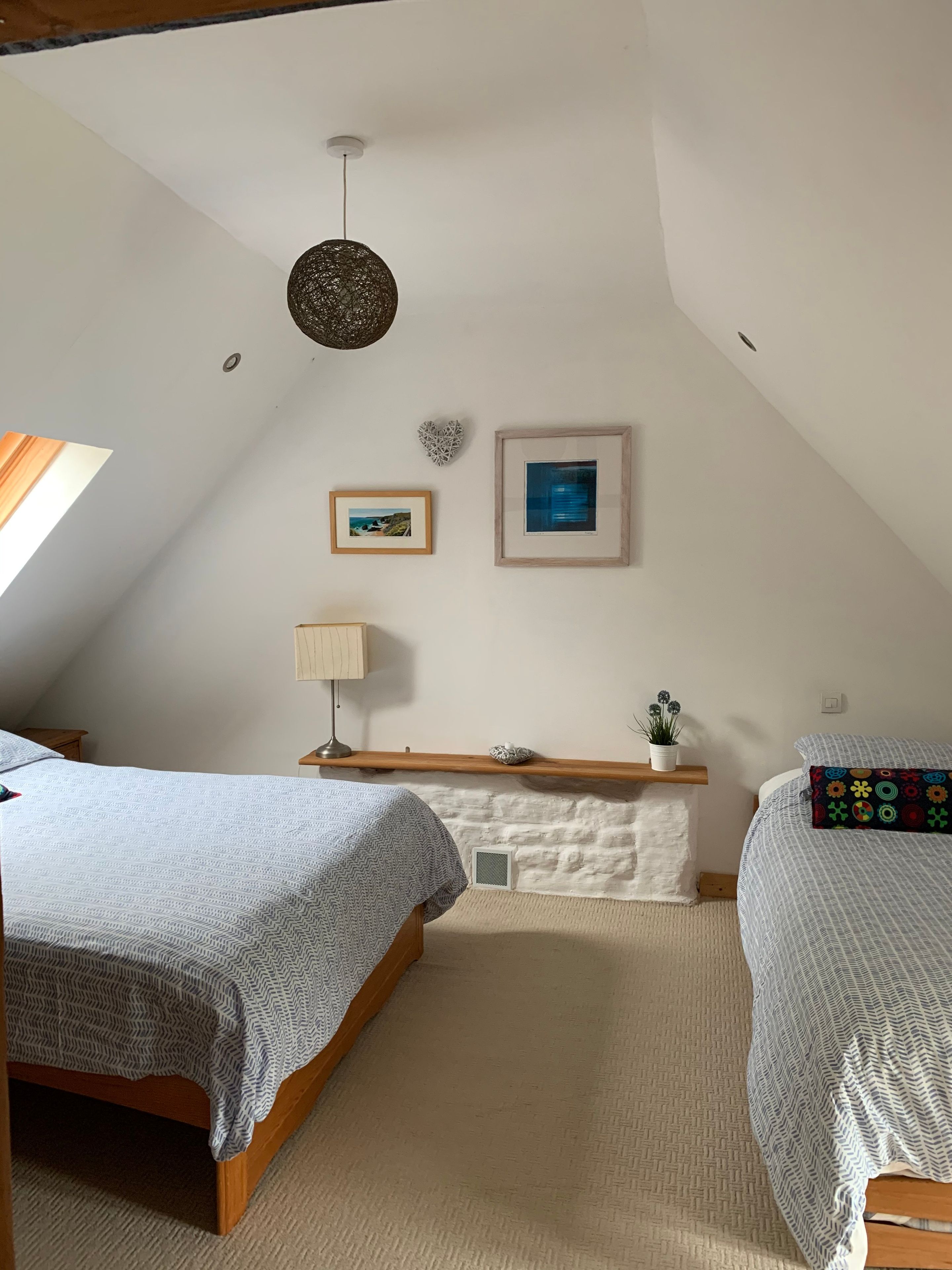 A bedroom with two beds, a wooden headboard, a white wall, and a ceiling light fixture.