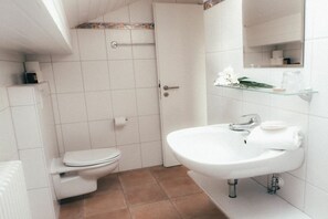 A bathroom with a white toilet, a sink with a mirror, and a shower area. - House Luna - Apartment Luna 4 (Schwangau)
