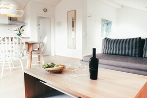 Ein modernes Wohnzimmer mit einer Couch, einem Esstisch mit Stühlen und einer Weinflasche.
