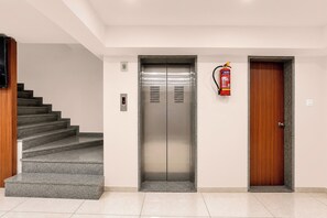 A modern elevator with a digital display, a fire extinguisher mounted on the wall, and a wooden door to the right. - Townhouse Oak Central Bus Station Rajkot (Rajkot)