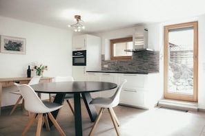 A modern kitchen with white cabinets, a black countertop, and a built-in oven. There is a dining table with two chairs and a vase with flowers. - House Luna - Apartment Luna 5 (Schwangau)