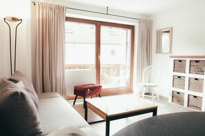 A modern living room with a sofa, a red ottoman, a white chair, a wooden table, and a large sliding glass door leading to a balcony. - House Luna - Apartment Luna 7 (Schwangau)