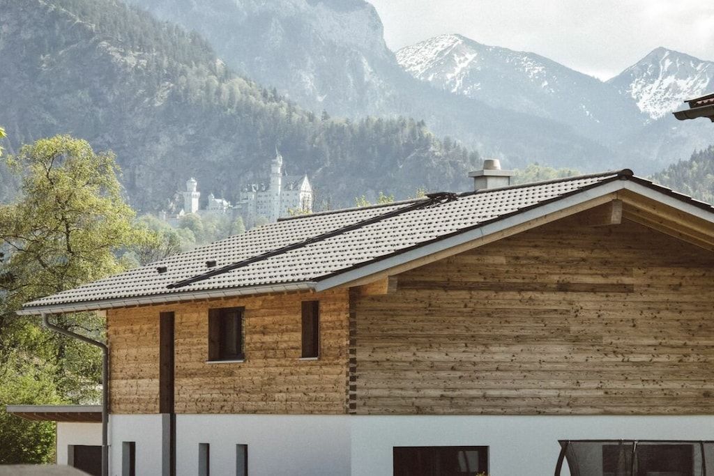 A wooden cabin with a sloped roof, set against a mountainous backdrop with a castle in the distance.