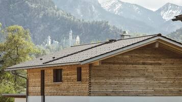 A wooden cabin with a sloped roof, set against a mountainous backdrop with a castle in the distance.