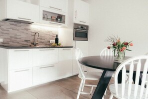 A modern kitchen with white cabinets, a dark countertop, and a dining area with white chairs. - House Luna - Apartment Luna 7 (Schwangau)