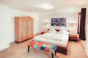 A bedroom with a bed, a wooden wardrobe, a bench, two bedside tables, a wall-mounted lamp, and a painting. - Luna Blanca - Apartment 2 (Schwangau)