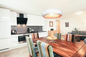 A modern kitchen with white cabinetry, a wooden dining table, and striped chairs. - Luna Blanca - Apartment 2 (Schwangau)