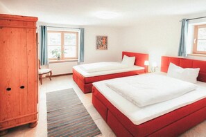 Ein Hotelzimmer mit zwei Betten, einem Holzschrank, einem Fenster mit Vorhängen, einem kleinen Tisch und einem Bild an der Wand.