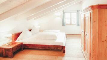Ein Schlafzimmer mit schrägem Dach, einem Bett, einem Nachttisch, einem Kleiderschrank und einem Fenster mit Vorhängen.