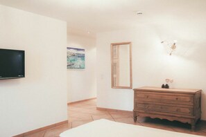 Een hotelkamer met een televisie, een houten dressoir, een spiegel en een schilderij aan de muur.