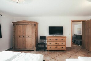Ein Zimmer mit einem Holzschrank, einem Fernseher auf einer Kommode, einem Sessel und einem Bett.