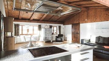A kitchen with a modern stove, a dining area with a table and chairs, and a living area with a sofa.